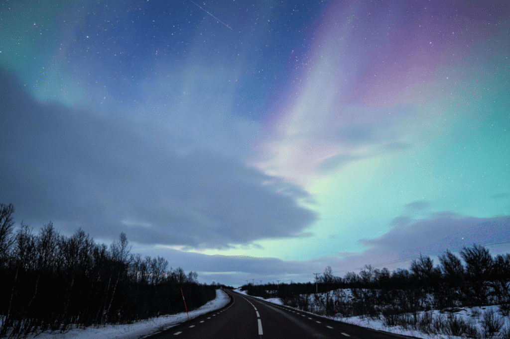 Winter road in Lapland with northern lights glowing above the treeline