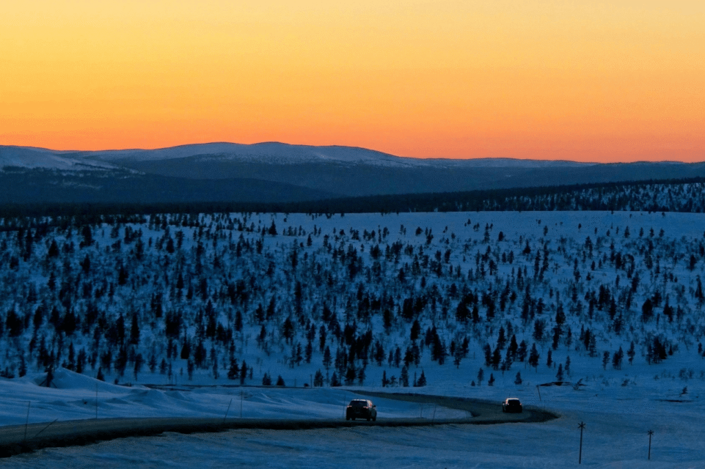 Transfer vehicle on a Lapland road at sunset with snow-covered fells in the distance