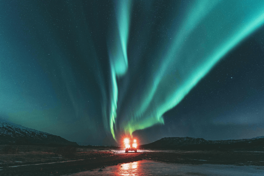 Private transfer vehicle driving at night under a strong green aurora display