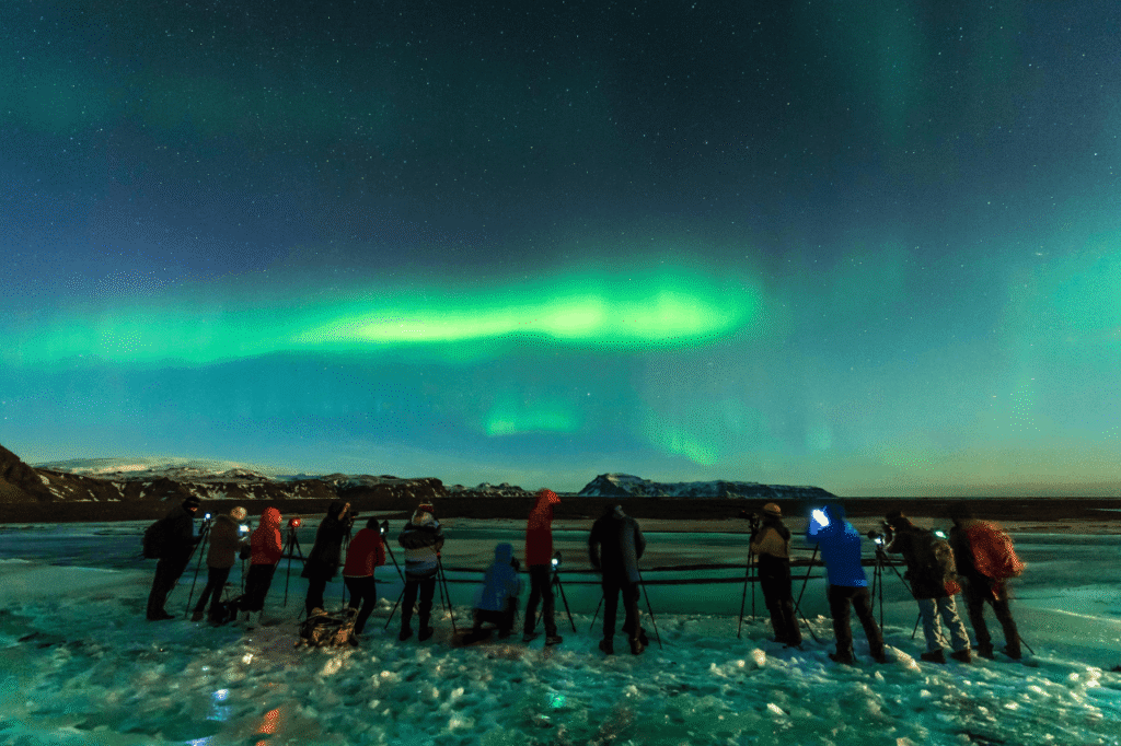 Northern lights tour group photographing the aurora over a frozen lake in Lapland