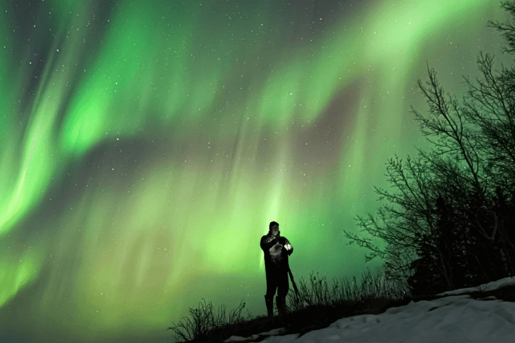 Guest standing under a bright green aurora borealis during a northern lights hunt